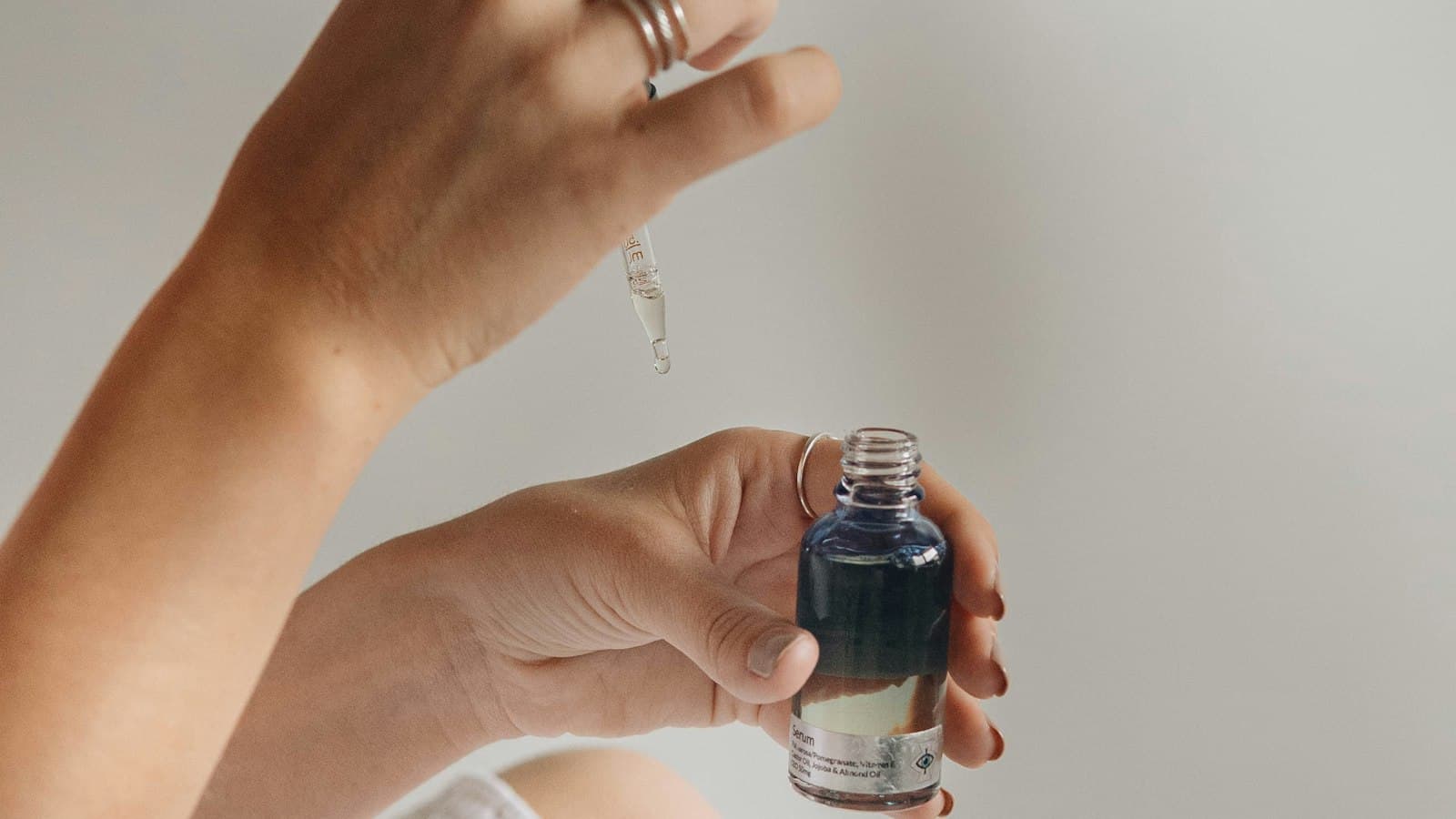 دستی که یک شیشه عطر کوچک را روی پارچه‌ی سفید نگه داشته